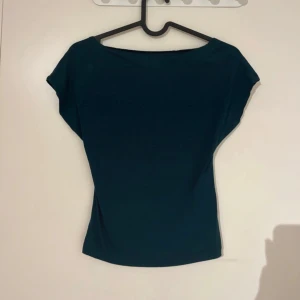 Mörkgrön topp med djup rygg - Säljer en mörkgrön topp med korta ärmar och en snygg djup urringning i ryggen. Toppen har en enkel och stilren design, perfekt att matcha med olika outfits. Materialet känns mjukt och följsamt.