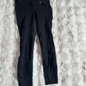 Svarta ridbyxor från CRW med helskodd - Svarta ridbyxor från CRW med helskodd i silikon för extra grepp. Byxorna har dragkedjeficka framtill. Snygg och funktionell design, perfekta för ridning. Pris kan diskuteras💞