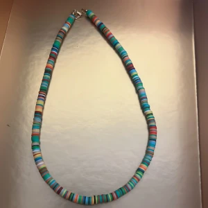 Färgglatt halsband med runda pärlor - Säljer ett halsband med platta, runda pärlor i olika färger som turkos, blå, orange och grön. Halsbandet har ett enkelt metallås och ger en lekfull och trendig känsla. Perfekt för att liva upp din outfit!