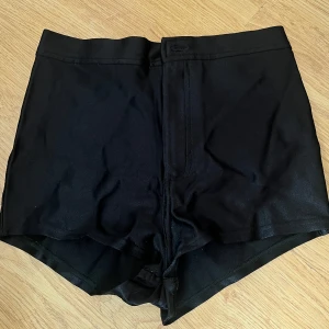 Svarta shorts från American Apparel - Svarta shorts från American Apparel med hög midja och klassisk design. De har två bakfickor, dragkedja och knapp framtill. Perfekta för sommaren och enkla att matcha med olika toppar.