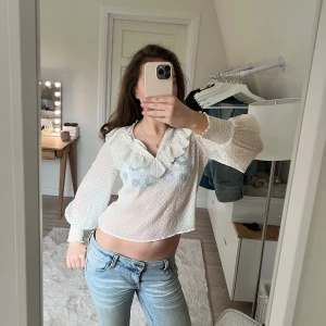 Vit blus med volang och spetsdetaljer - Säljer en söt vit blus med volangkrage och spetsdetaljer. Blusen har diskret prickigt mönster, v-ringning och långa ärmar. Perfekt för dig som gillar romantisk och feminin stil.💘🤩