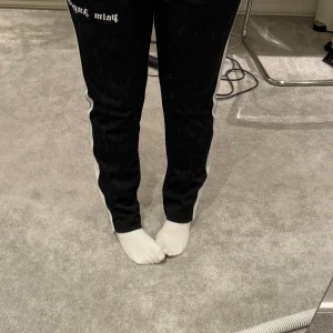 Svarta mjukisbyxor med vita ränder från Palm Angels - Svarta mjukisbyxor från Palm Angels med vita sidoränder och logga framtill. Byxorna har elastisk midja  knappt använda 