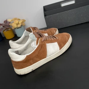 Valentino flycrew  - Snygga sneakers i brunt mocka med vita detaljer och vit sula. Skorna har snörning och en klassisk rund tå. Perfekta för dig som gillar stilrena och bekväma sko. Passar 42-44 