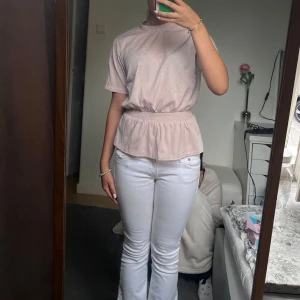 Ljusrosa blus med knyt i ryggen från Bubbleroom - Supersöt ljusrosa blus från Bubbleroom med resår i midjan och korta ärmar. Blusen har en fin knytdetalj i ryggen och är tillverkad i ett mjukt, tunt material. Perfekt för en feminin och stilren look. Den har en pytteliten fläck skriv privat om ni vill se!