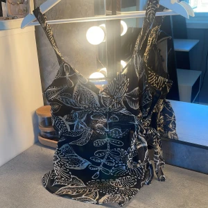 Svart och beige mönstrad linnetopp från Zara - Sitter som xs-xxs. Säljer en svart och beige linnetopp från Zara med tropiskt bladmönster. Toppen har smala axelband, omlottkänsla och knyt i sidan. Tillverkad i 100% polyester, perfekt för varma dagar.