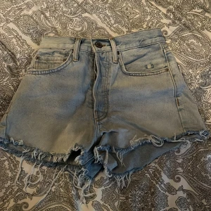 Ljusblå jeansshorts med fransar från Zara - Säljer ett par ljusblå jeansshorts från Zara med råa fransade kanter och klassisk femficksdesign. Shortsen har en avslappnad passform, perfekta för varma dagar. Snygga detaljer och slitningar för en trendig look. 