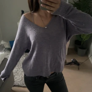 Ljuslila stickad v-ringad tröja - Mysig ljuslila stickad tröja med v-ringning och långa ärmar. Tröjan har en avslappnad passform och ribbade muddar vid ärmslut och nederkant. Perfekt för lager-på-lager och chill dagar.