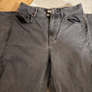 Grå jeansbyxor från H&M - Säljer ett par grå jeansbyxor från H&M i klassisk femficksmodell. Byxorna har raka ben och normal passform, tillverkade i bomull. Perfekta för en avslappnad stil, är också högmidjade. 