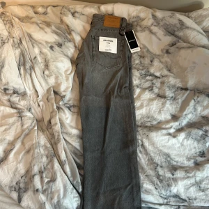 Grå jeansbyxor från Jack & Jones - Säljer ett par grå jeansbyxor från Jack & Jones i relaxed fit. Byxorna har klassisk femficksdesign, normalhög midja och raka ben. Perfekta för en avslappnad stil och passar till det mesta. Märkeslapp bak i midjan och etikett på bakfickan.