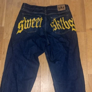 Blå jeans från Sweet SKTBS med gul text - Unika blå jeans från Sweet SKTBS med stor gul text på bakfickorna. Dom är lite slitna nere vid benen annars är dom helt okej