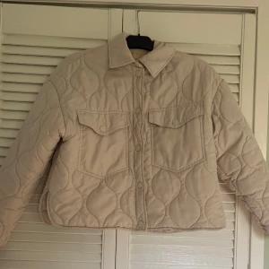 Beige quiltad jacka från Newyorker - Säljer en beige quiltad jacka från newyorker med tryckknappar framtill och två bröstfickor. Jackan har en klassisk krage.