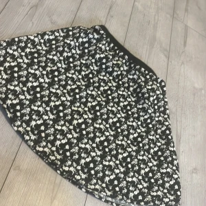 Svart blommig kjol från 157 - Säljer en svart kjol från 157 med vitt blommigt mönster. Kjolen har en bred svart resår i midjan och är lätt utställd. Perfekt för dig som gillar en klassisk men ändå söt stil. Använd ett fåtal gånger. Kjolen går typ ner till knäskolarna på mig (160cm lång)
