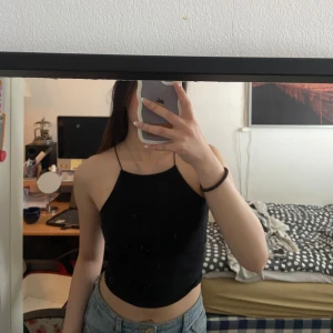 Svart croppad linnetopp - Säljer en svart croppad linnetopp med smala axelband och hög halsringning. Perfekt för varma dagar eller som ett lager under en skjorta. Enkel och stilren design som passar till mycket.