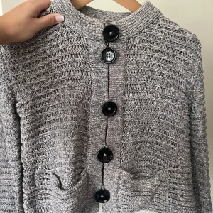 Grå stickad kofta med stora knappar - Säljer en grå stickad kofta från Dagmar med stora svarta knappar framtill. Koftan har två fickor och lång ärm, samt en lite croppad passform. Passar till allt! Hör av er vid frågor 🥰