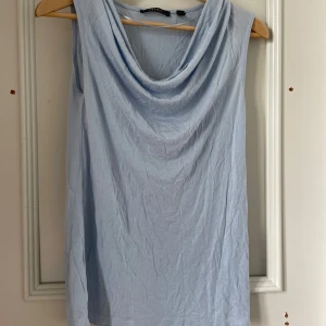 Ljusblå ärmlös topp med draperad hals från Esprit - Säljer en ljusblå ärmlös topp från Esprit med snygg draperad halsringning. Perfekt för varma dagar och enkel att matcha med både jeans och kjol. Mjuk och skön bomullskänsla.