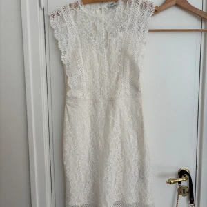 Vit spetsklänning  - Superfin vit spetsklänning från ONLY i storlek XS. Klänningen har vackra spetsdetaljer, är ärmlös med volangkant och har en feminin v-ringning. Perfekt för sommaren tillfällen, skolavslutningar oxh studenten. Klänningen är endast andvänd en gång. 