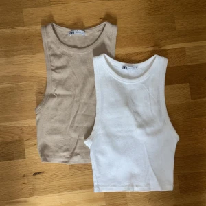 Två ribbade linnetoppar från Zara - Säljer två croppade ribbade linnetoppar från Zara i färgerna beige och vit. Perfekta för sommaren och enkla att matcha med olika outfits. Båda är ärmlösa och har rund halsringning.