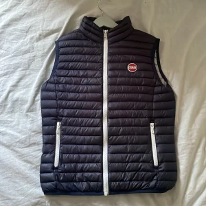 Navieblue väst från Colmar - Snygg blå dunväst från Colmar med vita dragkedjor och logotyp på bröstet. Västen har två fickor framtill och quiltad design som ger en grischig look. Perfekt att bära över en hoodie eller t-shirt