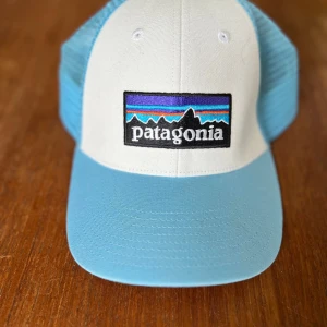 Blå och vit keps från Patagonia - Snygg keps från Patagonia i ljusblått och vitt med klassisk logga framtill. Kepsen har mesh-bakstycke för extra ventilation och justerbar snapback. Perfekt för soliga dagar och outdoor. Klpt men aldrig använd. 😅