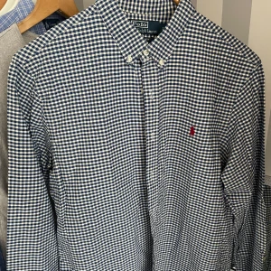 Blårutig skjorta från Polo Ralph Lauren - Säljer en blårutig skjorta från Polo Ralph Lauren i slim fit-modell. Skjortan har långa ärmar, klassisk krage med knappar och en liten röd broderad logga på bröstet. Perfekt för dig som gillar stilrena och tidlösa plagg.