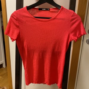 Ribbad röd topp från Bik Bok - Säljer en ribbad röd topp från Bik Bok i storlek XS. Toppen har korta ärmar och rund halsringning. Perfekt för dig som gillar enkla och stilrena plagg med lite edge. Ngn noppa se bild. 