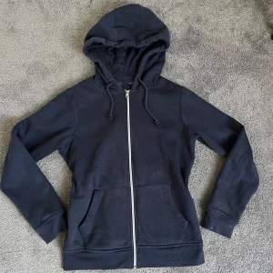 Mörkblå zip up hoodie - En klassisk mörkblå hoodie med dragkedja framtill och två fickor. Tröjan har huva med dragsko och långa ärmar. Perfekt för en avslappnad stil.