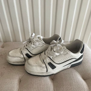 Vita sneakers med svarta detaljer - Säljer ett par vita sneakers med svarta detaljer och snörning. Skorna har perforerade partier på ovandelen och en platt sula. Perfekta för en avslappnad och sportig stil.☺️skriv för frågor eller mer bilder