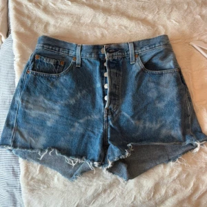 Levi's 501 jeansshorts - Säljer ett par klassiska blå Levi's 501 jeansshorts med knappar framtill. Shortsen har fem fickor och en vintage tvättad look. Perfekta för sommaren. Storleken är W28.