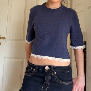 Mörkblå croppad tröja med spetsdetaljer - Säljer en mörkblå croppad tröja med trekvartsarmar och vita spetsdetaljer vid ärmslut & nederkant. Tröjan är gjord av ett fint merino ull och jag har sytt på spetsen själv.