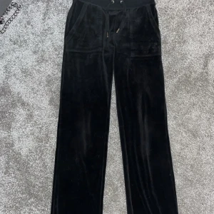 Svarta Juicy Couture byxor - Mysiga svarta velourbyxor från Juicy Couture med dragsko i midjan och fickor både fram och bak. Byxorna har en relaxed passform och är perfekta för en chill och trendig look.