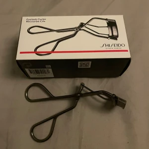 Ögonfransböjare från Shiseido - En klassisk ögonfransböjare i metall från Shiseido. Den har ergonomiska handtag och en böjd form som passar de flesta ögonformer. Perfekt för att lyfta och forma fransarna för en mer öppen blick. Levereras i originalförpackning.