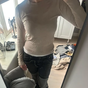 Beige  tröja med guldigaknappar - Säljer en beige ribbad tröja med rund halsringning och långa ärmar. Tröjan har dekorativa knappar vid ärmsluten och sitter tight på kroppen. Perfekt för lager-på-lager och enkel att matcha.