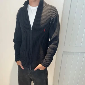 Mörkblå ribbad kofta från Ralph Lauren - Säljer en stilren mörkblå ribbad kofta från Ralph Lauren med dragkedja och röd logga på bröstet. Den ser ut och vara svart dock pga ljuset. Perfekt för kyligare dagar och enkel att matcha med olika outfits. Storlek M. Skick 8/10. Hör av er vid eventuella frågor😊⭐️