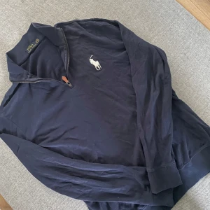 Mörkblå långärmad tröja med dragkedja från Polo Ralph Lauren - Säljer en mörkblå långärmad tröja från Polo Ralph Lauren med halv dragkedja och klassisk krage. Tröjan har en broderad vit logga på bröstet och är tillverkad i mjuk bomull. Perfekt för en stilren och avslappnad look.