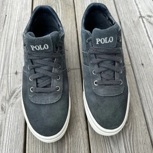 Svarta sneakers från Polo Ralph Lauren - Snygga svarta sneakers från Polo Ralph Lauren med vit sula och klassisk logga på sidan. Skorna har snörning och är tillverkade i mocka med textilfoder. Nypris 1299