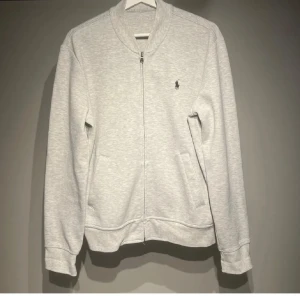 Ralph Lauren zip - Säljer en stilren ljusgrå ziptröja från Ralph Lauren med diskret logga på bröstet. Tröjan har långa ärmar, dragkedja framtill och två fickor. Perfekt för sommarkvällar🤩 priset är diskuterbart😁