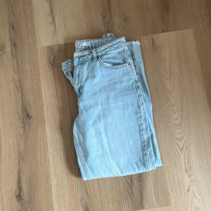 Ljusblå jeansbyxor från NA-KD - Säljer ett par ljusblå jeans från NA-KD i klassisk femficksmodell. Jeansen har raka ben med råa, fransiga benslut och hög midja. Perfekta för en avslappnad och trendig look.