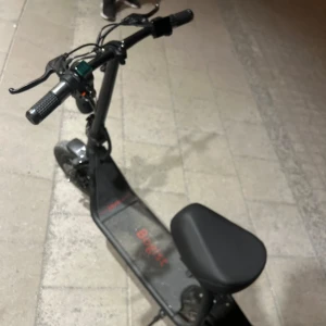 Svart elscooter med sadel - Säljer en svart elscooter med bekväm sadel och digital display på styret. Scootern har breda handtag, fotplatta och robust ram. Perfekt för smidig transport i stan.