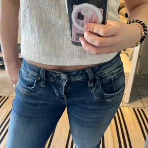 Blå jeans från LTB Valerie - Säljer ett par klassiska blå jeans från LTB, modell Valerie. Jeansen har normal passform, bootcut model och snygga slitningar framtill. Perfekta till vardags och har en tidlös look med utsvängda ben och låg midja. Storlek 27/30
