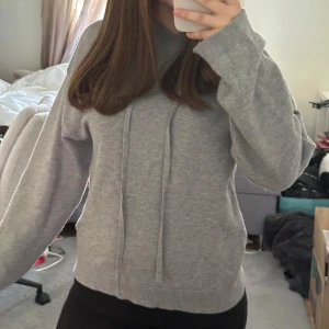 Grå hoodie med dragsko - Säljer en enkel och stilren grå hoodie med huva och dragsko. Tröjan har långa ärmar och ribbade muddar vid ärmslut och nederkant. Perfekt för en avslappnad look.