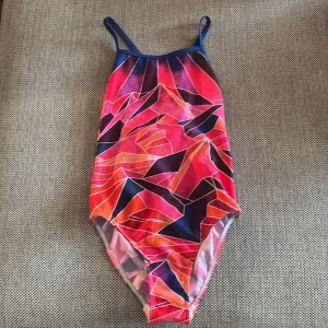 Färgglad baddräkt från Funkita - Säljer en baddräkt från Funkita med ett coolt grafiskt mönster i rött, rosa, orange och blått. Modellen har smala axelband och öppen rygg med knyt. Perfekt för simträning eller strandhäng! Använd fåtal gånger. Strl 12 år. 152.