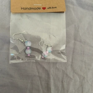 Handgjorda örhängen med pastellfärgade pärlor - Säljer ett par handgjorda örhängen med runda pärlor i pastellfärger, främst ljusblått, vitt och rosa. Pärlorna är trädda på silverfärgade krokar. Perfekta för att ge en söt och unik touch till din stil.💕