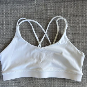 Vit sport-bh med korsade band - Säljer en vit sport-bh med tunna korsade axelband i ryggen. Perfekt för träning eller som ett snyggt basplagg. Mjukt och stretchigt material som sitter skönt mot kroppen.