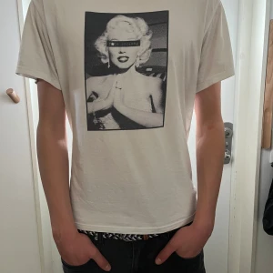 Vit t-shirt med tryck - Säljer en vit t-shirt med ett svartvitt tryck av en ikonisk person på framsidan. T-shirten har korta ärmar och en normal passform. Perfekt för en avslappnad stil. Den är från onewear..