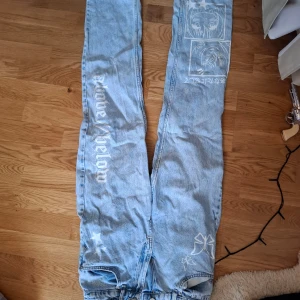 Ljusblå jeans med anime-tryck från Soya fashion - Unika ljusblå jeans från Soya fashion med coolt anime-tryck och textdetaljer. Perfekta för dig som vill sticka ut med en kreativ stil. Jeansen har en normal passform och är tillverkade i denim.