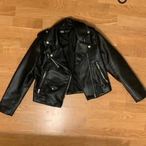 Black Leather Jacket from Zara - Stylish black leather jacket from Zara with zippers and classic biker style. The jacket has long sleeves and two zippered pockets and sleeve ends. Perfect for a cool look.