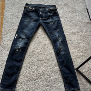 Mörkblå jeans från Dsquared2 - Snygga mörkblå jeans från Dsquared2 med coola slitningar och färgstänk. De har en slim passform och är tillverkade i denim. Perfekta för en trendig look!