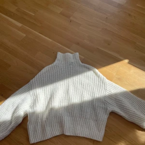 Vit stickad tröja från H&M Divided - Säljer en mysig vit stickad tröja från H&M Divided. Tröjan har en hög krage och ribbade detaljer vid ärmslut och nederkant. Perfekt för kyliga dagar!