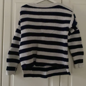 Randig stickad tröja - Säljer en mysig stickad tröja med breda ränder i marinblått och vitt. Tröjan har en avslappnad passform med långa ärmar och en rund halsringning. Perfekt för kyliga dagar!