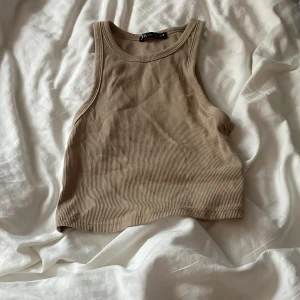 Beige ribbad linnetopp från Zara - Säljer en snygg beige ribbad linnetopp från Zara. Toppen är ärmlös och har en stilren design som passar perfekt till sommaren. Perfekt för en avslappnad look eller att styla upp med accessoarer.
